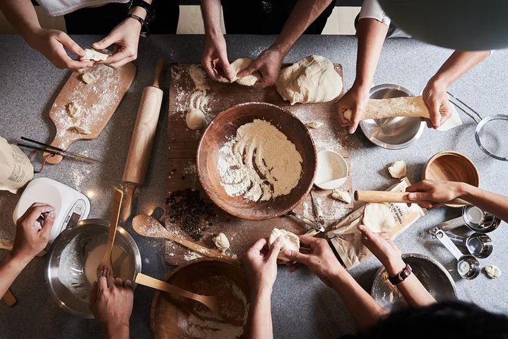 Multiple people making dough around a table.